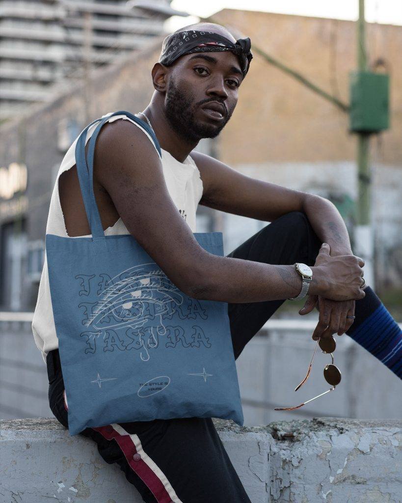 tote bag mockup of a cool guy sitting on a concrete fence 29451