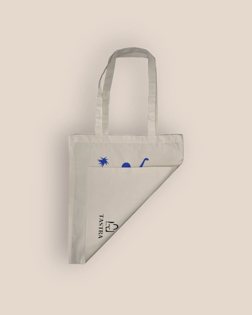 Achterzijde van de naturelkleurige Abstract Free Spirited Tote Bag, naar voren gevouwen om het merklogo in het midden te tonen