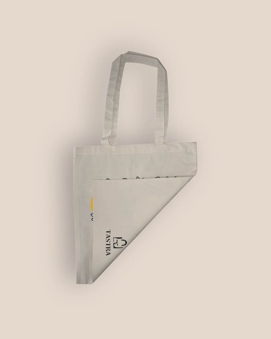 Achterzijde van de naturelkleurige Cat Adventure Tote Bag, naar voren gevouwen om het Tastra logo in het midden te tonen