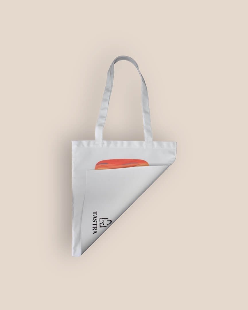 Achterzijde van de witte Scream Alien Painting Tote Bag, naar voren gevouwen om het Tastra-logo onderaan in het midden te tonen